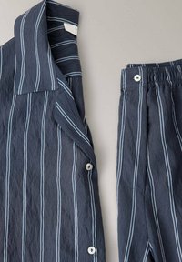 Ensemble de pyjama bleu marine à rayures verticales blanches, comprenant une chemise à col boutonnée et un pantalon assorti avec taille élastique sur un fond clair.
