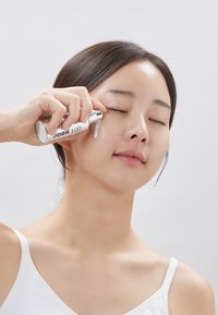 Fuktgivande serum i en silver cylindrisk flaska märkt "DRN 100." Klar gel appliceras nära det slutna ögat; sval hud, minimal distraktion.