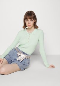 Top de malha canelada verde menta com gola e detalhes em botões, combinado com calções de ganga de cintura alta, acompanhados por um cinto estampado.