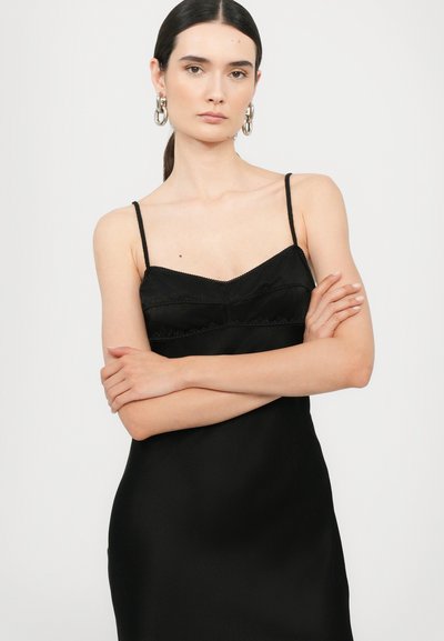 Vestido de seda negro con tirantes finos, textura suave, encaje en la parte superior y un corte ajustado.