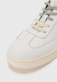 Hvite lærsneakers med rund tå, grå og kremfargede lisser, og kontrasterende sømdetaljer. Glatt tekstur, minimalistisk design.