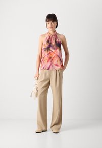 Halterneck-Top in pink und lila Batikmuster, kombiniert mit beige weitem Hose und beige Schuhen. Das Top hat ein geknotetes Design am Hals.