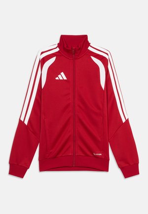 Rdeča športna jakna z zadrgo po celotni dolžini, z belimi črtami na rokavih, belimi ramenskimi paneli in belim logotipom na levi strani prsnega koša, položena ravno na belem ozadju.