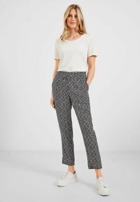 Pantaloni a righe in bianco e nero con un design affusolato, dotati di tasche laterali, indossati con una maglietta beige chiaro e sneakers bianche.