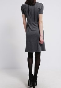 Kortärmad grå klänning med vertikala sömmar, en figursydd livdel, utsvängd kjol och dekorativa stygn längs ryggen, matchad med ankelstövlar.