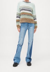 Gestreifter Strickpullover in Mintgrün, Weiß, Grau und Braun. Kombiniert mit hellblauen Schlagjeans und schwarzen Schuhen mit dicker Sohle.