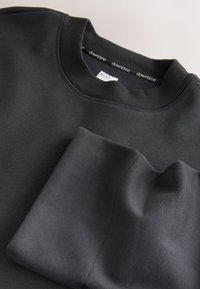 Schwarzer Pullover mit geripptem Halsausschnitt und weicher Textur. Der gefaltete Bereich zeigt eine glatte Oberfläche mit sichtbaren Nahtdetails.