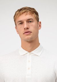 Witte katoenen polo met een relaxte pasvorm, zachte textuur, drie knopen aan de voorzijde en een kraag. Geschikt voor casual draagstijl of voor het laagjes dragen.