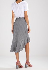 Jupe midi vichy noir et blanc avec un ourlet volanté, associée à un t-shirt blanc et des talons roses à brides avec un talon en marbre.