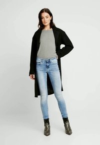 Μαύρο μακρύ παλτό πάνω από γκρι τοπ, συνδυασμένο με ανοιχτό μπλε skinny τζιν και μαύρες μπότες αστραγάλου με σχέδιο φίδι.