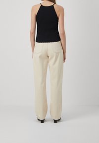 Haut halter noir à côtes associé à un pantalon ample couleur crème. Le pantalon présente des poches arrière, une texture subtile et une coupe droite.
