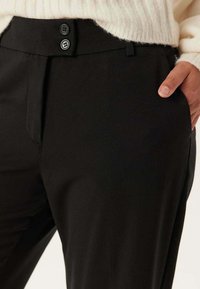 Černé kalhoty s hladkým materiálem, slim fit střih, dva knoflíky v pase a postranní kapsy pro praktičnost.