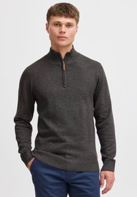 Dark grey zip-up sweater made of textured knit material, featuring a high collar and ribbed cuffs. Accented with a small leather tag.