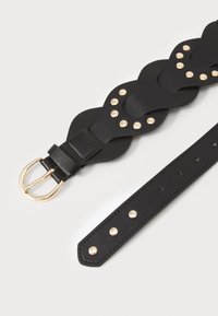 Cinturón de cuero negro con un diseño ondulado, adornado con tachuelas doradas y una hebilla rectangular. La correa tiene agujeros distribuidos de manera uniforme para ajustes.