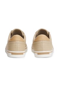 Paire de baskets décontractées beiges vues de dos, avec des semelles blanches et une petite étiquette de marque sur chaque talon.