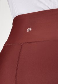 Leggings bordeaux a vita alta realizzati in tessuto elasticizzato con cuciture piatte. Presentano un piccolo logo bianco sulla cintura.
