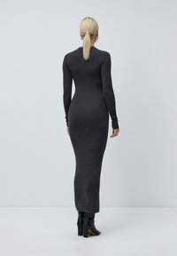 Šedé maxi šaty s dlouhým rukávem z žebrovaného úpletu, přiléhavý střih, vysoký límec, bezšvový design, spárované s černými botami.