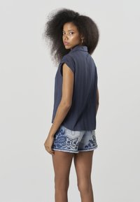 Top albastru marin cu mâneci scurte, dintr-un material texturat și cu guler, asortat cu pantaloni scurți din denim deschis cu broderie florală albastră și margini nefinisate.