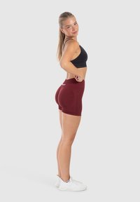 Donkergrijze sportbeha en bordeauxrood compressiekorte broek. De shorts hebben een hoge tailleband en een gladde textuur. Witte sportschoenen.