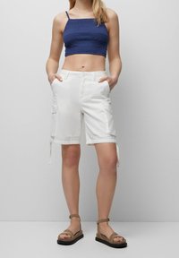 Hvide cargo shorts med sidelommer og justerbare benremme. Parret med en navy crop top med et struktureret design og tynde stropper.