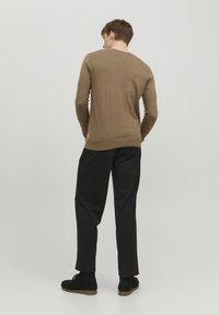 Brun strikkegenser med rund hals, lange ermer og ensfarget tekstur, kombinert med svarte stoffbukser og mørke sko.