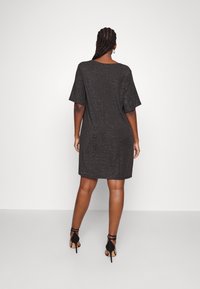 Schwarzes kurzes Kleid mit lockerem Schnitt und kurzen Ärmeln, das eine subtile schimmernde Textur aufweist. Kombiniert mit schwarzen Riemchen-High Heels.