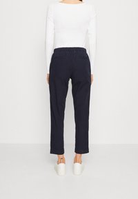 Tmavě modré teplákové kalhoty s elastickým pasem, dvěma zadními kapsami a zužujícími se nohavicemi, doplněné bílými nazouvacími botami. Hladká textura látky.