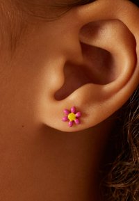 Bloemvormige knopoorbel, met een ontwerp van roze bloemblaadjes en een centrale gele parel. Het materiaal lijkt glanzend met een gladde textuur.