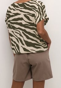 Krótki rękaw top w kolorze beżowym z zielonymi paskami w zebry, połączony z brązowymi szortami. Top ma luźny krój i teksturowany materiał.