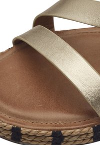Guldmetallisk sandal med korsremmar, brunt läderinlägg och vävd jute-yttersula med marinblå detaljer. Mjuk yta.