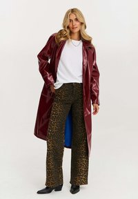 Lesklý burgundský dlhý kabát cez biely tričko, doplnený hnedými nohavicami s leopardím vzorom a širokými nohavicami, spolu s čiernymi členkovými čižmami, s výrazne definovanými líniami.