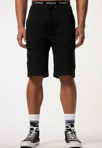 Shorts cargo noirs avec poches latérales, une taille élastique avec cordon, et une bande logo. Associés à des baskets montantes noires et des chaussettes à motifs.