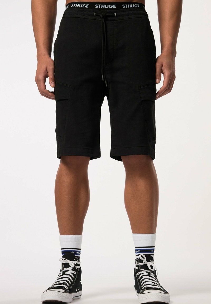 Shorts cargo noirs avec poches latérales, une taille élastique avec cordon, et une bande logo. Associés à des baskets montantes noires et des chaussettes à motifs.