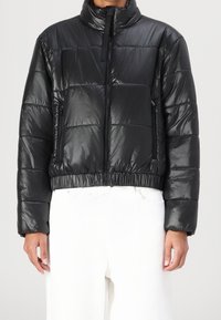 Czarna pikowana kurtka puchowa o błyszczącym wykończeniu. Posiada wysoki kołnierz, zamek błyskawiczny i elastyczny dół. Kwadratowy fason z przeszyciami.