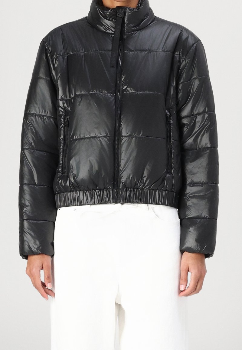 Czarna pikowana kurtka puchowa o błyszczącym wykończeniu. Posiada wysoki kołnierz, zamek błyskawiczny i elastyczny dół. Kwadratowy fason z przeszyciami.