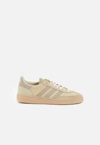 Beige Wildledersneaker mit drei horizontalen beigen Streifen, strukturierten hellbraunen Akzenten und gelbem "Spezial"-Logo. Flache Gummisohle.