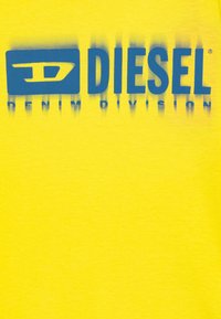Gul bomulls t-skjorte med en blå "DIESEL" logo og teksten "DENIM DIVISION", med en gradienteffekt som går fra blått til gult.