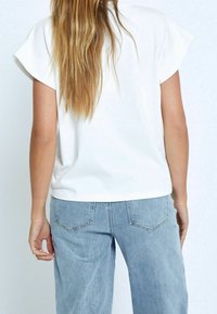 Bílé tričko s krátkým rukávem a rovný střih, vyznačující se hladkou texturou. Nosit se se světle modrými, volnými džíny ze denimu s detaily kapes.