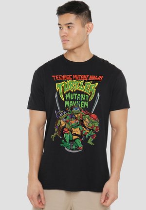 Man wearing black Teenage Mutant Ninja Turtles "Mutant Mayhem" graphic t-shirt with four turtles in action poses on front.