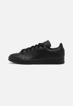 Zapatillas negras de cuero con un acabado suave, que presentan cordones redondos, acentos laterales perforados y una suela de goma texturizada.