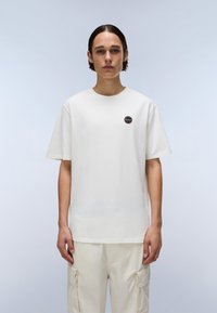 Tricou alb din bumbac, cu guler rotund, mâneci scurte și un mic logo circular pe pieptul stâng. Textură netedă și croială lejeră.