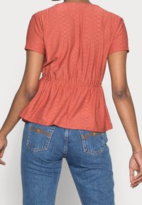 Pellava pääntie, jossa on tekstuurinen kangas ja timanttikuvio, lyhyet hihat ja elastinen keräys vyötäröllä.