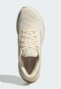 Beige sportschoen met een ademend mesh bovenwerk, vetersluiting, gevoerde kraag en gestructureerde zool. Heeft een logo op de tong en in de binnenkant.