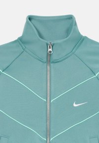 Light green zip-up jacket with a high collar, featuring a textured material, contrasting light blue accents, and a small white logo.