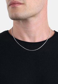 Närbild av en mans nacke som bär ett tunt silverhalsband över en svart T-shirt med rundad hals.
