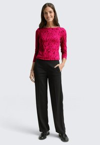 Fuchsias langärmliges Oberteil mit strukturiertem Muster, kombiniert mit hoch taillierten schwarzen Hosen und schwarzen Schuhen; moderner, taillierter Schnitt.