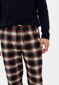 Pantaloni da pigiama in flanella con una fantasia a quadri marrone, blu navy e bianca, con vita elastica e lacci; leggeri e morbidi al tatto.