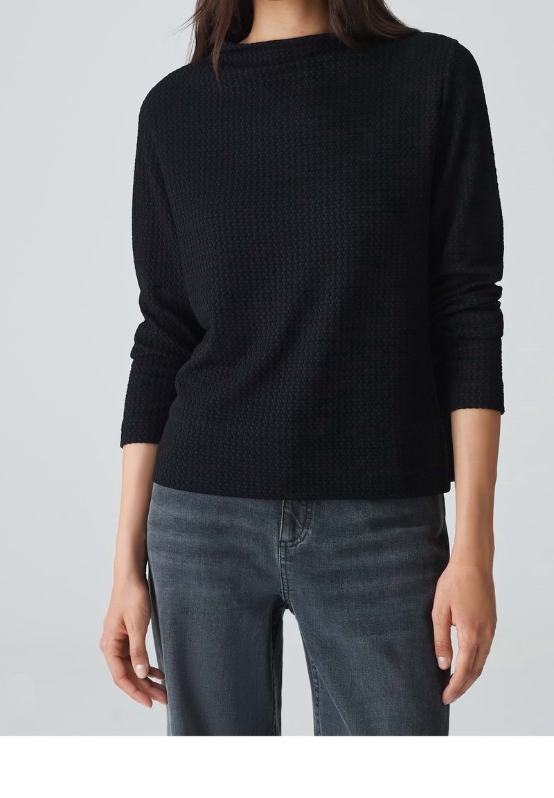 Pull noir texturé à manches longues et col rond, associé à un jean gris foncé. Le tissu présente un motif tissé subtil.