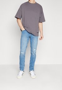 Grå kortärmad t-shirt med lös passform, ihopparad med ljusblå jeans med slitna detaljer och vita sneakers med svarta ränder.