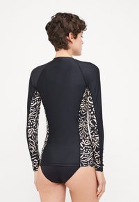 Black long-sleeve rash guard featuring floral-patterned accents in beige along the sides, made from stretchy, lightweight material.